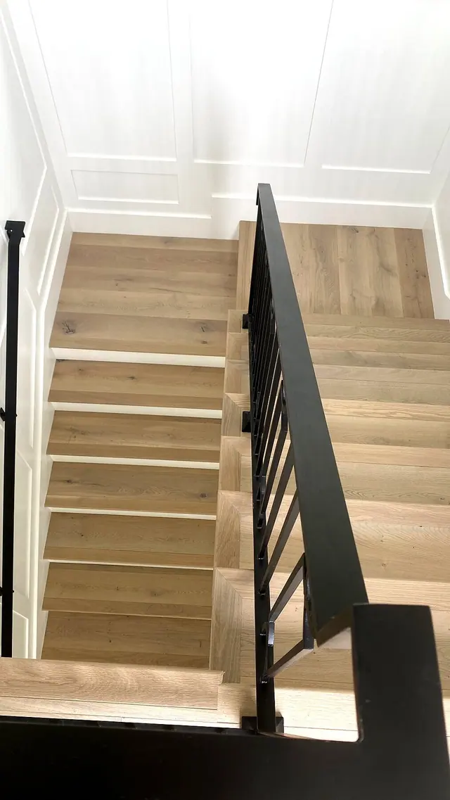 Light oak staircase installation with black railing and white wall paneling