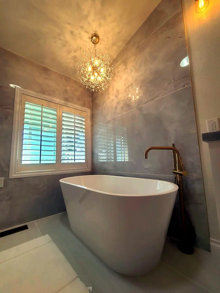 Luxury bathroom remodel with freestanding tub, chandelier, and tile walls by Grain and Stain Renovations
